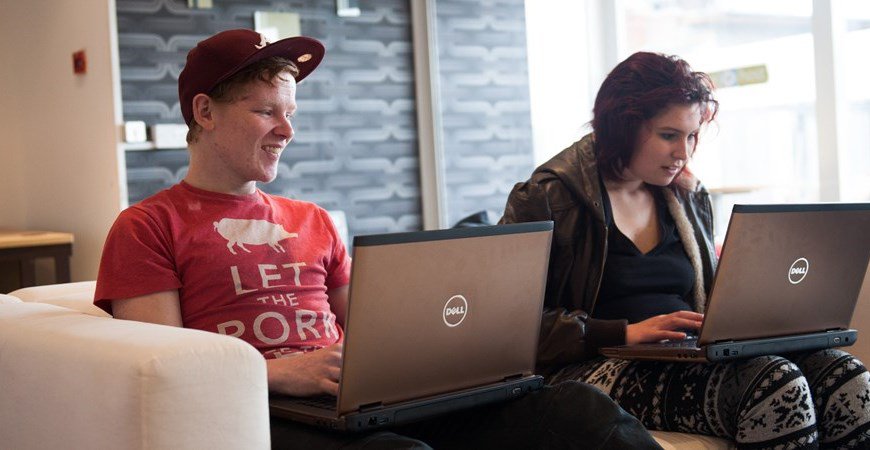 Teenage girl and boy sitting on sofa with laptops