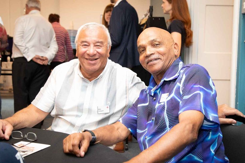 Two older men sitting at a table smiling for a photo