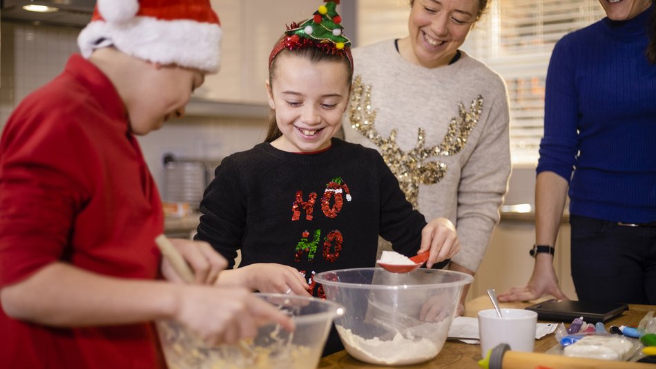 A family wearing Christmas jumpers and novelty Christmas items, baking together in the kitchen
