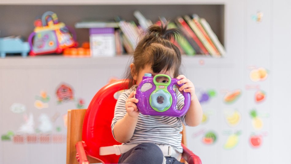 Toddler sitting in high chair and playing with toy camera