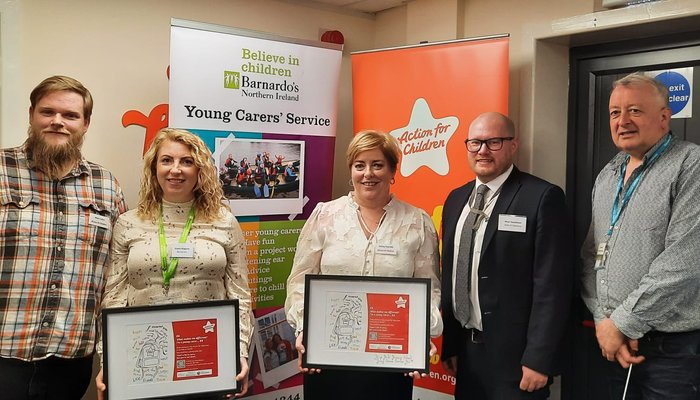 Five adults standing in front of Barnado's and Action for Children pull up banners, two of them holding framed posters