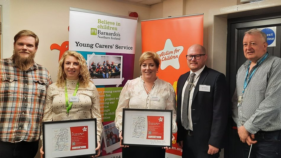 Five adults standing in front of Barnado's and Action for Children pull up banners, two of them holding framed posters