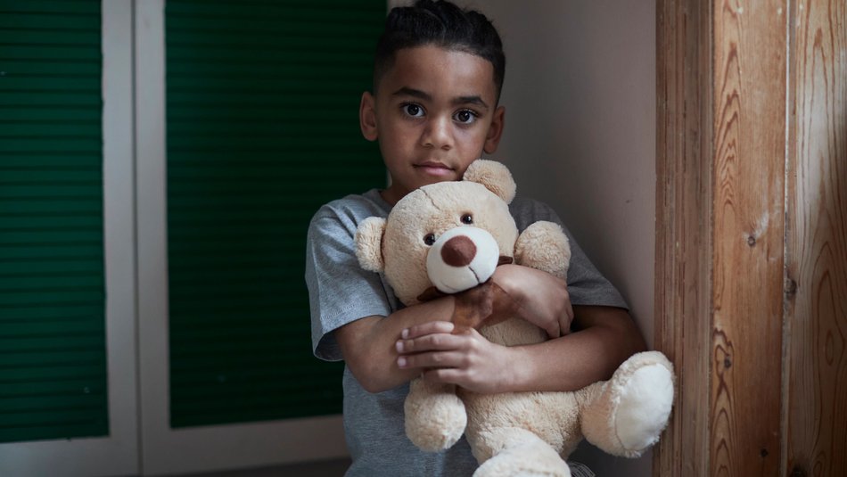 Boy looking into the camera holding a teddy bear