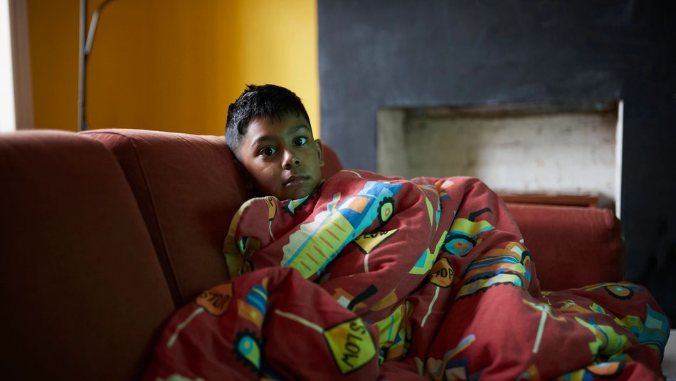 Boy looking into the camera with a worried face covered by a blanket
