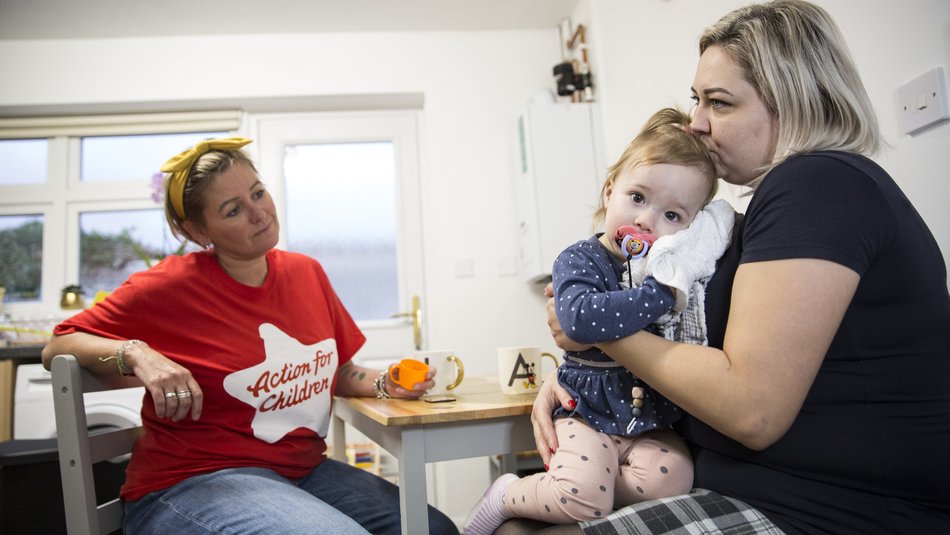 Natalia and Chloe sit at a kitchen table with Action for Children worker Kirsty