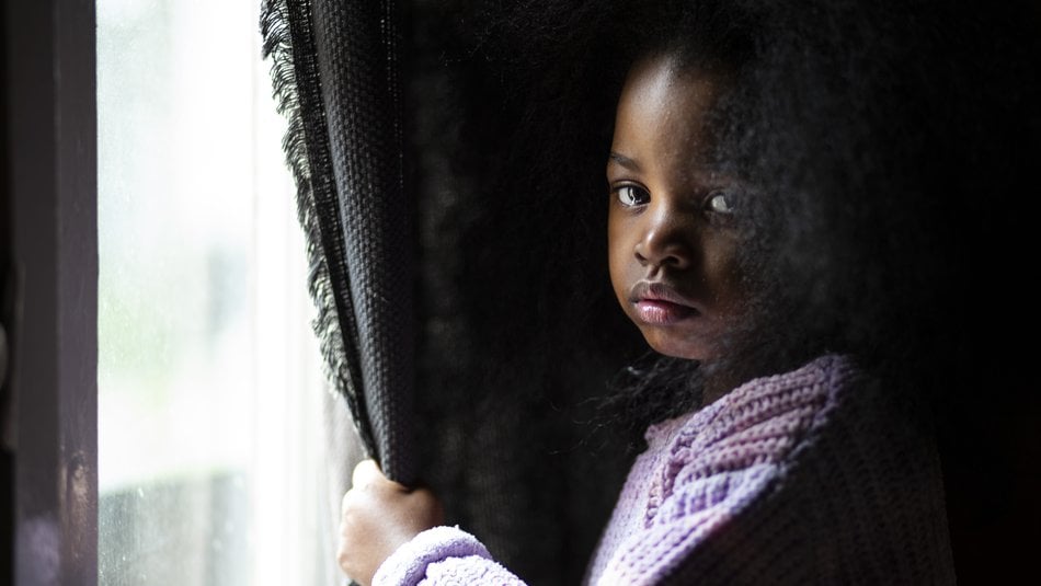 Alice, a sad young girl stands at the window while looking into camera