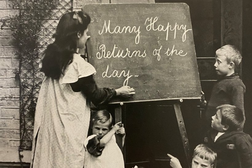 Black and white photograph of children writing on a chalk board