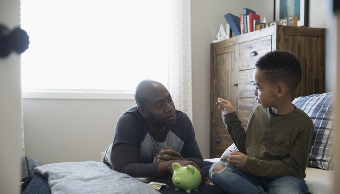 Dad sitting on bed with son and piggy bank