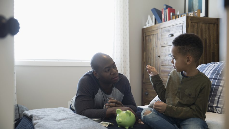 Dad sitting on bed with son and piggy bank