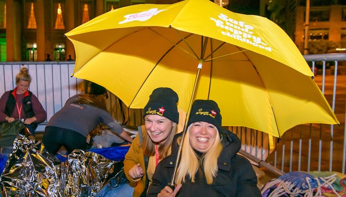 Two women at Boycott your Bed in their sleeping bags holding an umbrella - crop 4