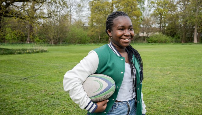 Esther smiling, holding a rugby ball under her arm