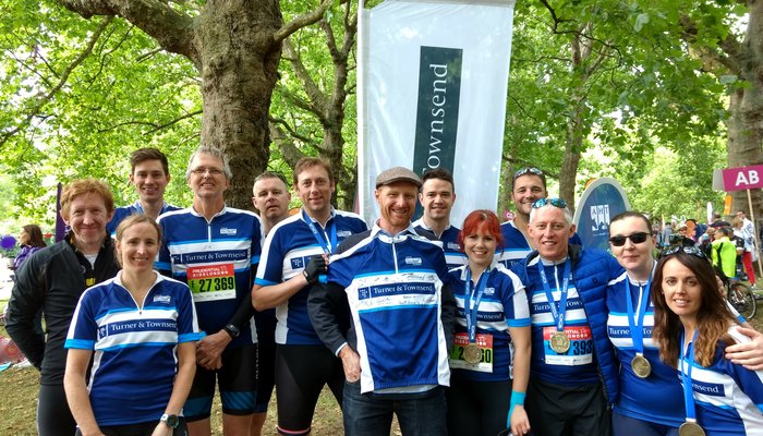 Group of people stanidng under some trees, wearing Turner & Townsend branded cycling tops