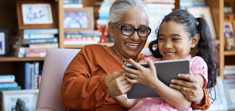 Happy grandmother with smiling daughter on lap reading iPad