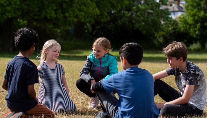 Happy group of young kids sitting in a circle in the park