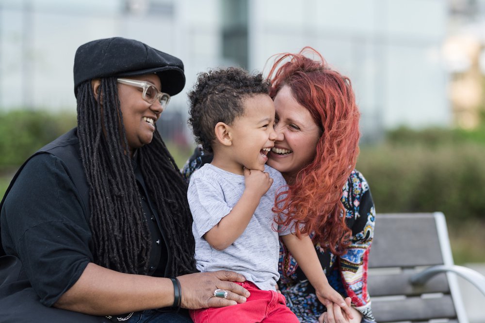 Happy mothers sitting and laughing on a bench with young son