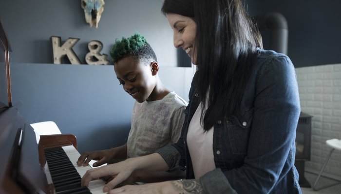 Happy woman and young girl sat playing piano together
