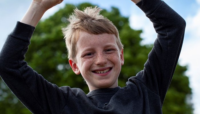 Happy young boy throwing arms in the air and smiling at the camera