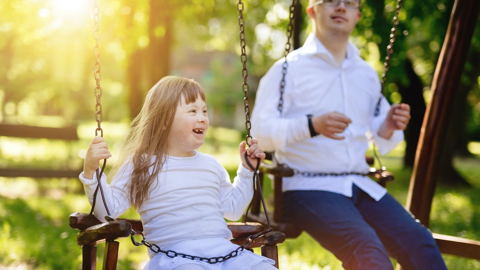 Happy young sister and older brother playing on the swings