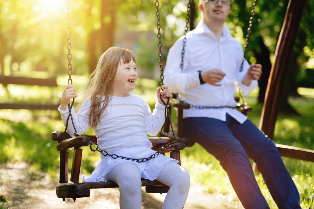 Happy young sister and older brother playing on the swings