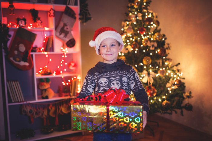 Boy carrying Christmas present in front of Christmas tree
