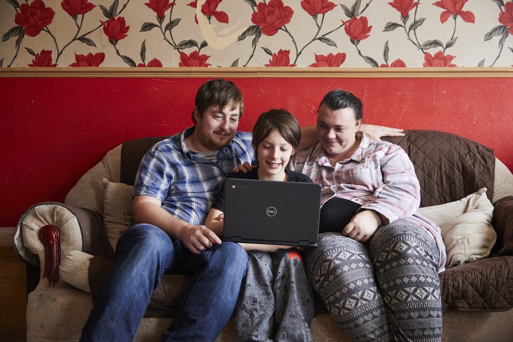 Jacob sitting on a sofa with both his parents with his laptop