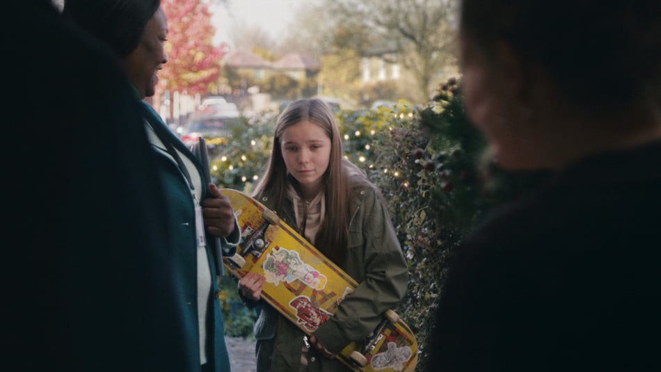 Young girl holding skateboard standing at the door look down at floor as she meets her new foster carers in John Lewis Christmas Ad