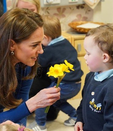 Kate Middleton kneeling down to hand flower to child at Ballymena Sure Start Childrens Centre