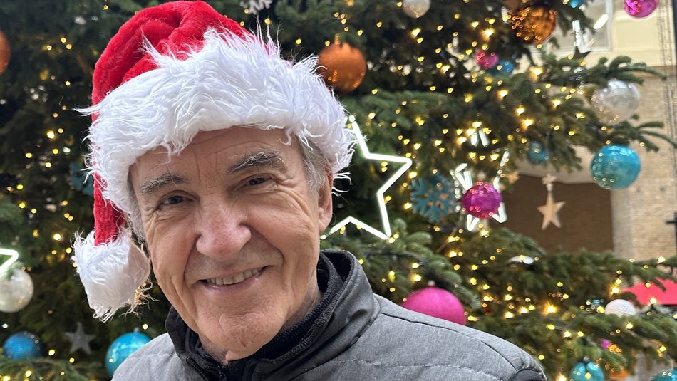 Larry Lamb against Christmas tree and wearing a Santa hat