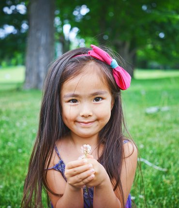 Little girl with long hair standing in field holing flower
