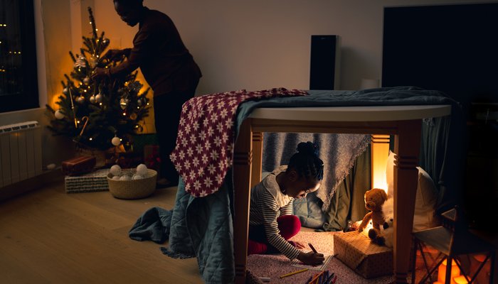 little girl writing down Christmas wish list under the table, in an improvised tent