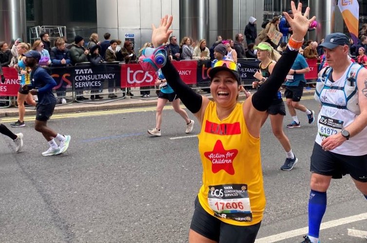 Woman running and cheering at the London Marathon whilst running for Action for Children