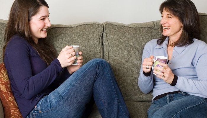 Mother and teenage daughter sitting on sofa and drinking tea together
