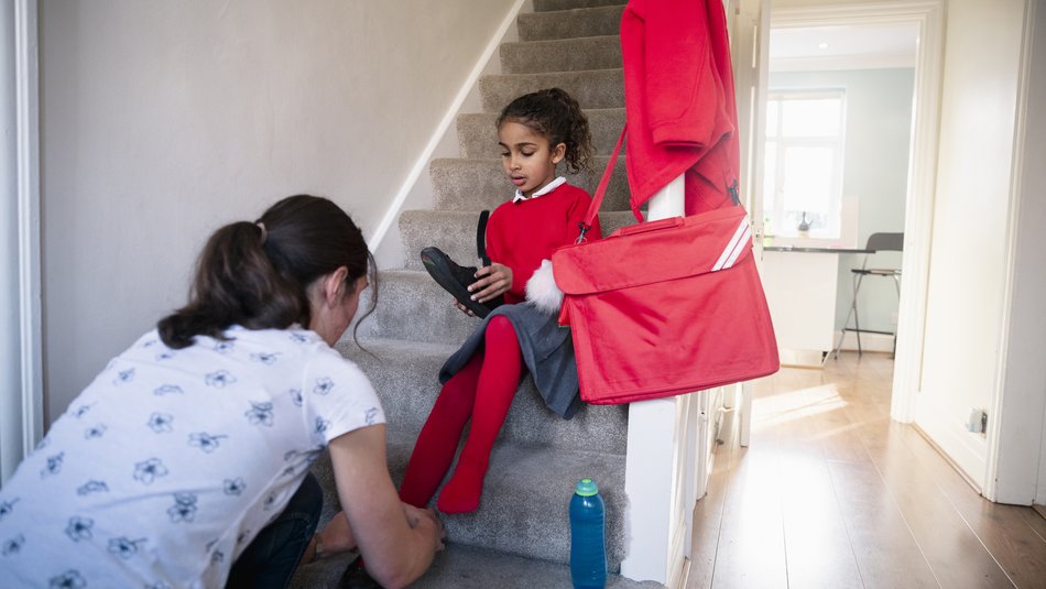 Mother helping her daughter put on school shoes
