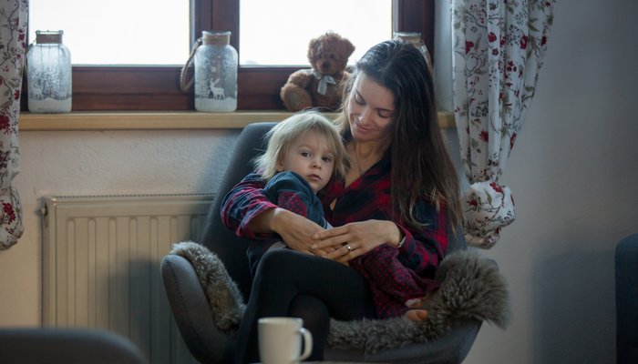 Mother sitting on chair in living room and holding child on lap looking to camera