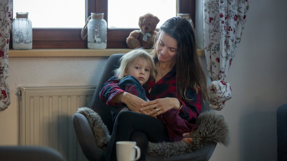 Mother sitting on chair in living room and holding child on lap looking to camera