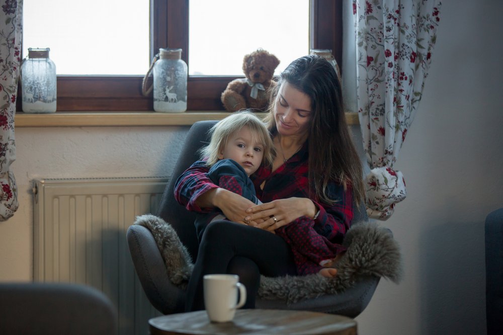 Mother sitting on chair in living room and holding child on lap looking to camera