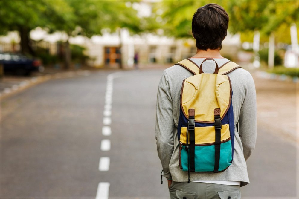 Rear view of teenage boy with backpack walking down the street and looking to the future