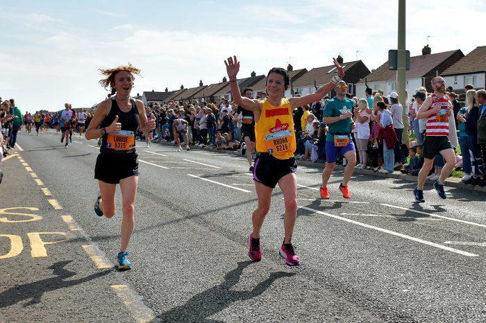 Rhona, woman in Action for Children t-shirt, cheers to the crowd as she runs the great north run for Action for Children