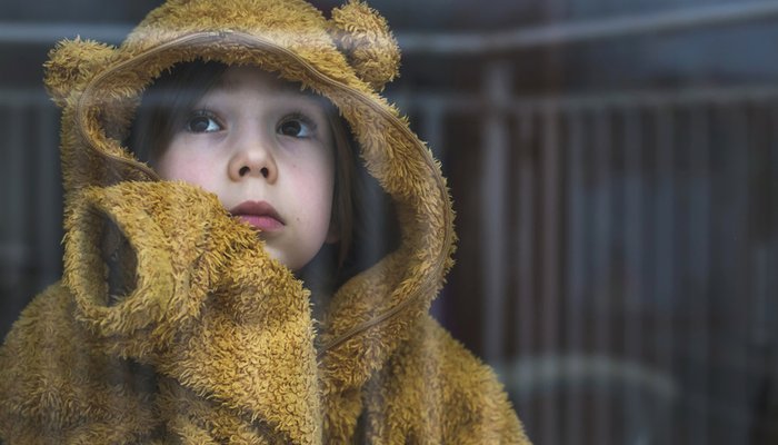 Sad cold child wearing yellow jumper looking out window