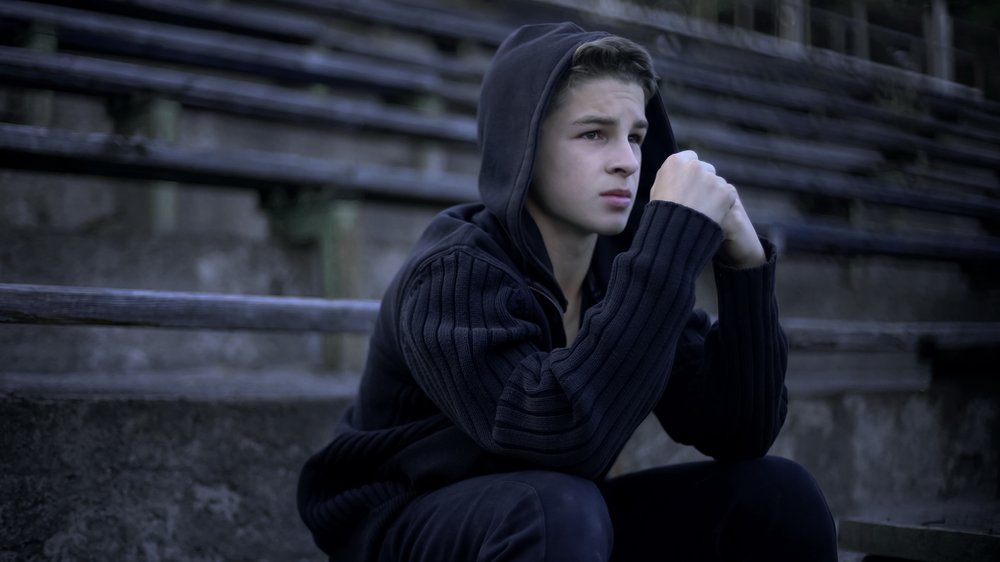 Boy sitting outside looking into the distance in a grey atmosphere