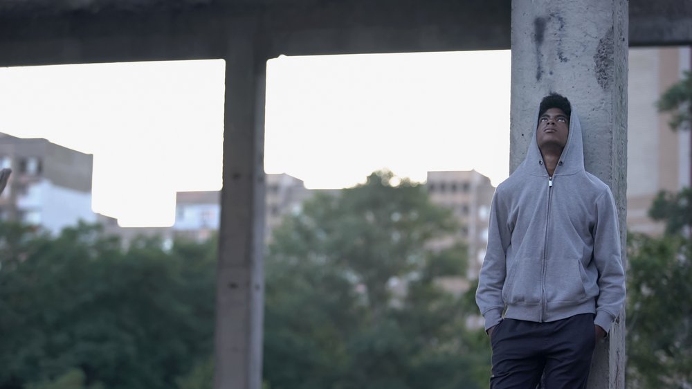 Boy standing amongst concrete pillars - trees surround - he looks up at sky