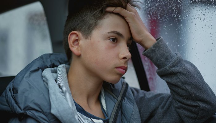 Boy looking out window thinking whilst its raining outside
