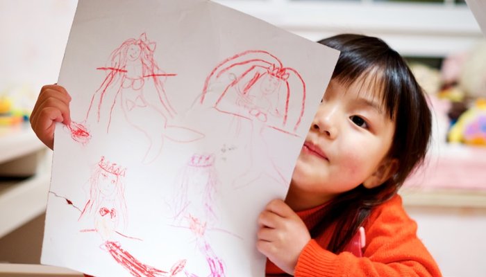 Small girl in cot holding up drawing of mermaids
