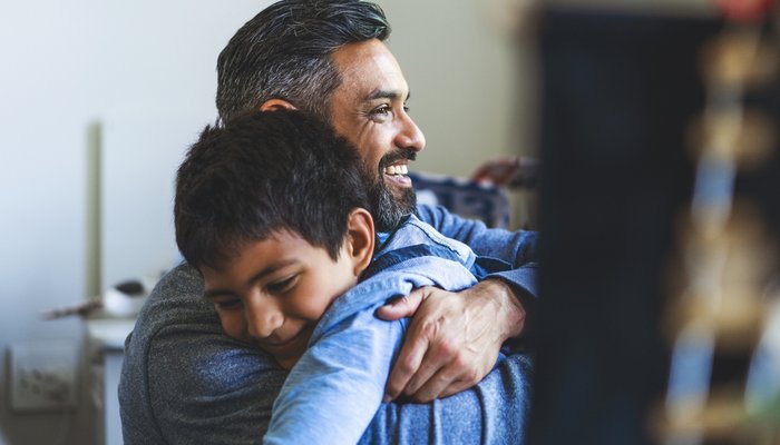 Smiling man embracing boy in bedroom. Happy father is looking away with son at home. They are spending leisure time