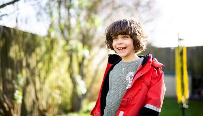 Smiling young boy outside wearing a red coat.
