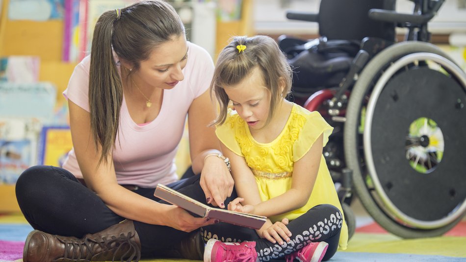 Teacher and young girl sitting on the ground reading a book together.jpg