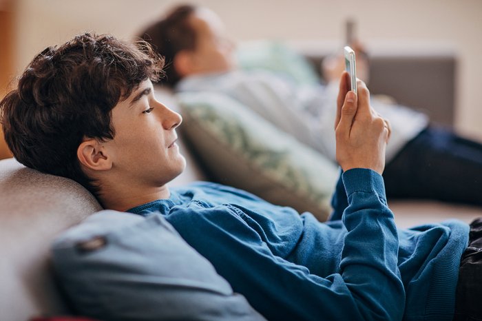 Teen boy sitting on sofa in living room using a mobile phone