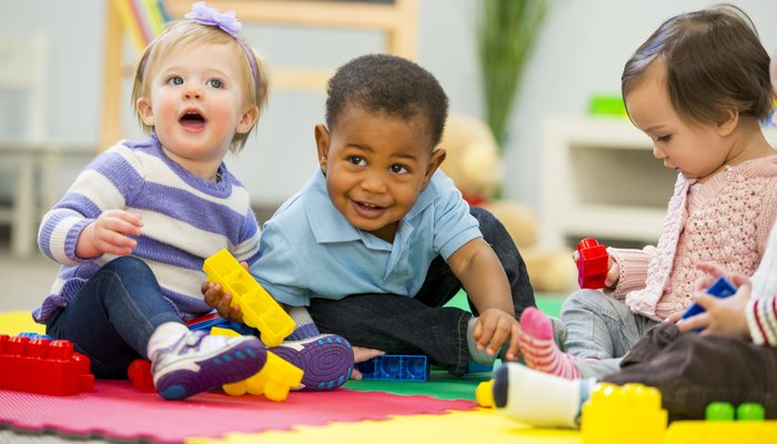 three babies sitting on a colourful mat playing with toy blocks.jpg