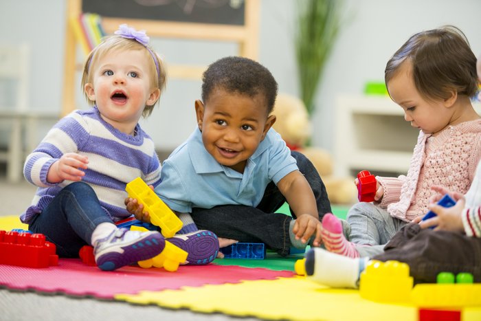 three babies sitting on a colourful mat playing with toy blocks.jpg