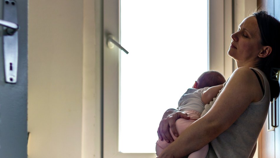 tired mother leans against kitchen wall, while rocking child to sleep